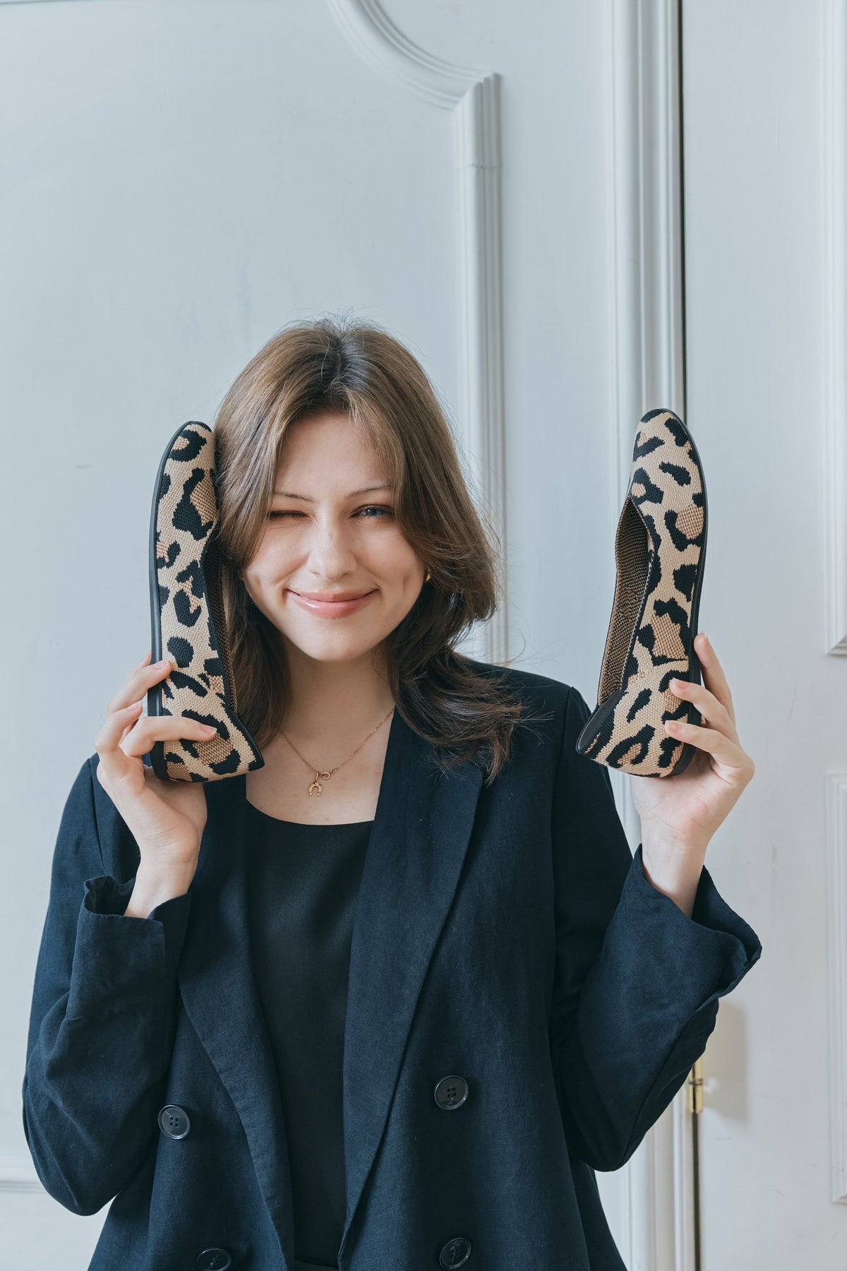 Frau hält zwei a.soyi Strickschuhe im Leo-Muster neben ihr Gesicht